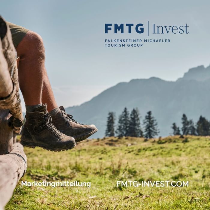 Beine auf Holz sitzend, Berg und Bäume im Hintergrund, FMTG Invest Logo und Website-Text.