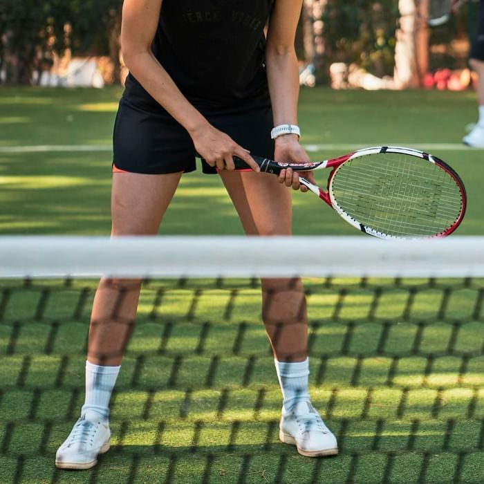 Tennisspielerin mit Schläger am Netz, bereit für Aufschlag auf grünem Rasenplatz.