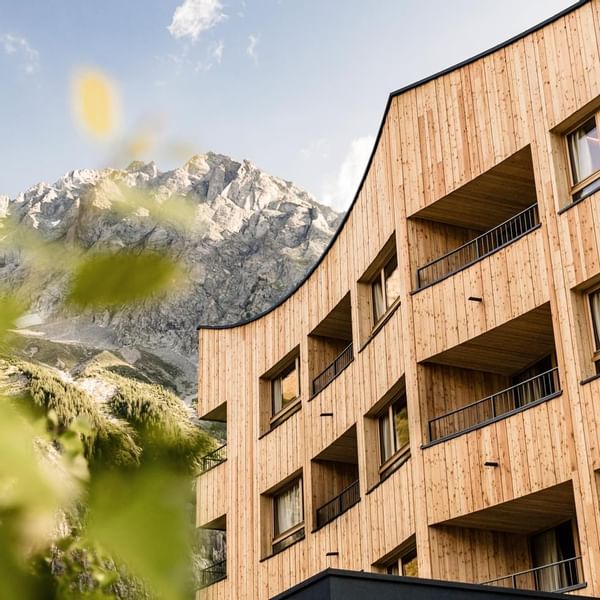 Modernes Holzgebäude mit Balkonen vor einem Berg in einer bewaldeten Umgebung.