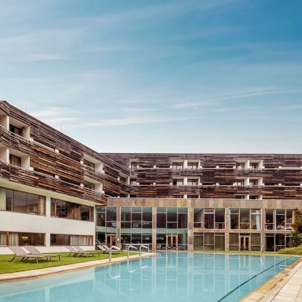 Modernes Hotelgebäude mit Außenpool und Liegestühlen unter einem blauen Himmel.
