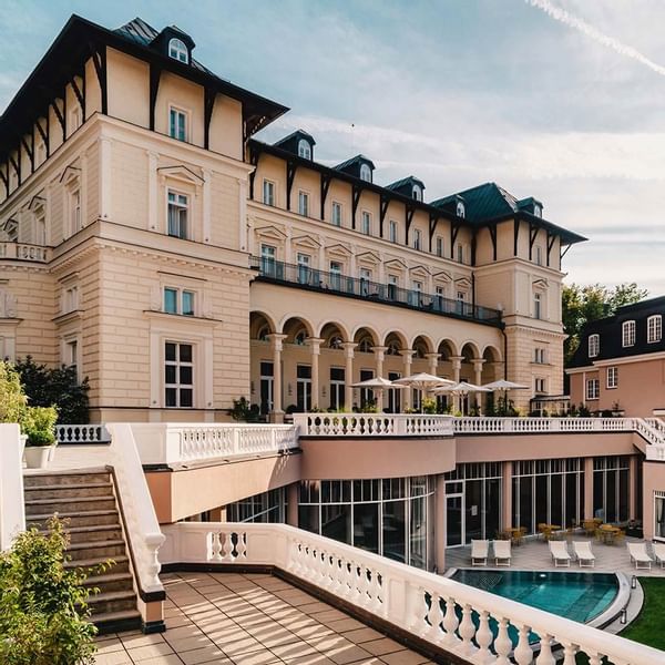 Elegantes Gebäude mit Terrasse, Pool und weißen Liegen unter Sonnenschirmen vor blauem Himmel.
