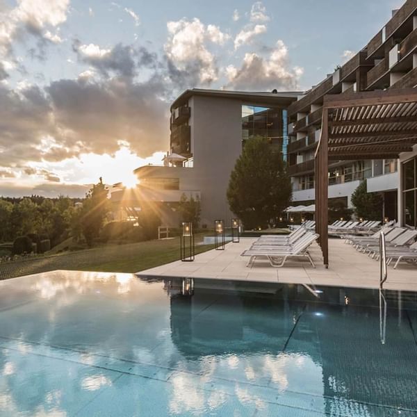 Außenpool eines modernen Hotels mit Liegen und Sonnenschirmen, umgeben von Bäumen und Gebäuden.