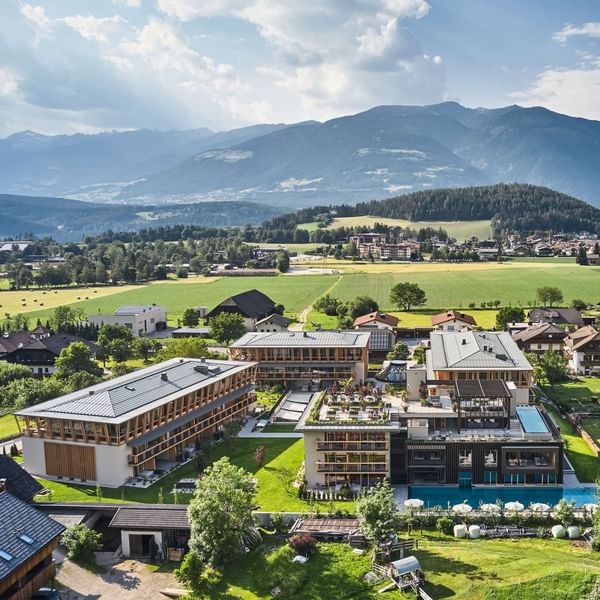 Luftaufnahme eines modernen Hotels mit Schwimmbad, umgeben von Feldern und bewaldeten Bergen.
