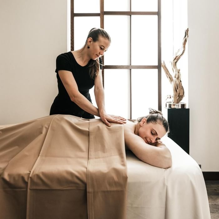 Eine Masseurin führt eine Rückenmassage an einer Frau auf einem Massagetisch durch.