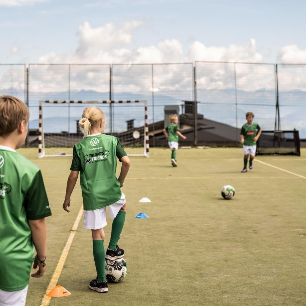 Kinder in grünen Trikots trainieren auf einem Fußballfeld mit Toren und Trainingshütchen.