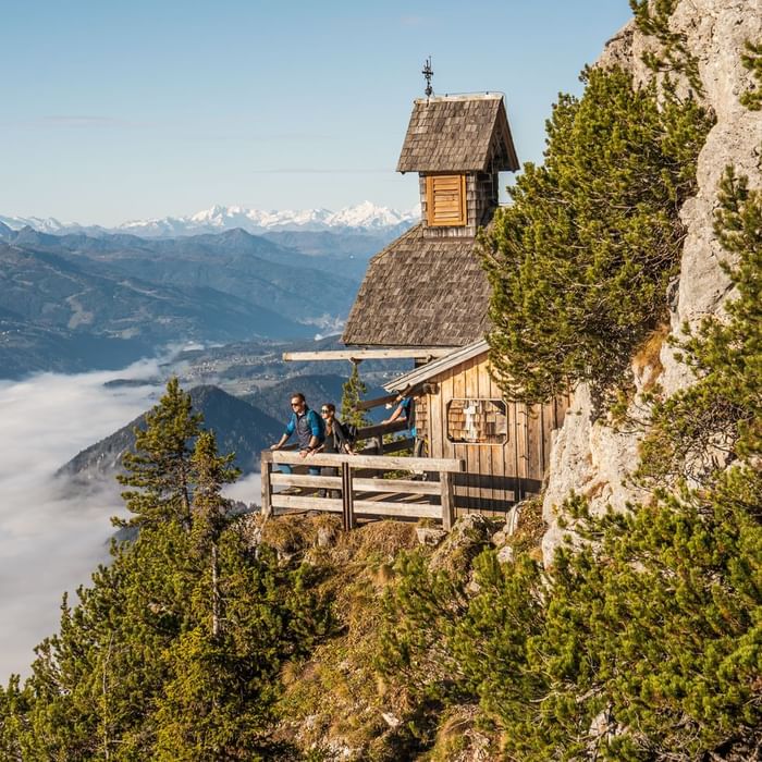 Coppia di escursionisti in cima a una montagna con una piccola cappella di legno.