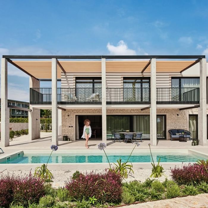 Moderne Villa mit Pool und Terrasse, umgeben von Pflanzen und Möbeln, an einem sonnigen Tag.