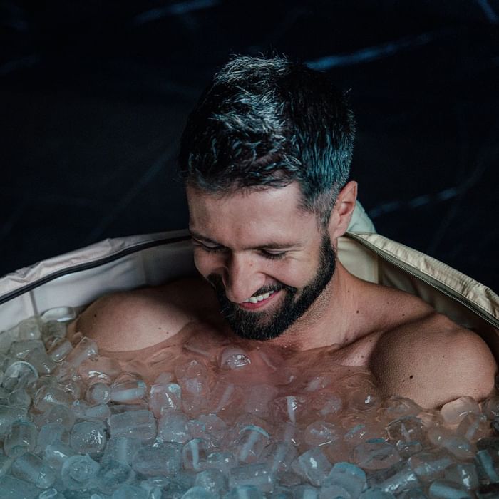 Bärtiger Mann mit dunklem Haar genießt eine Eisbad-Therapie in einem aufblasbaren Becken.