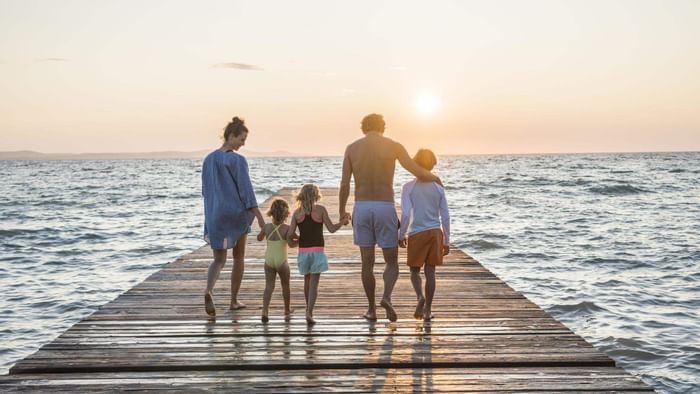 Familie genießt den Sonnenuntergang auf einer hölzernen Seebrücke, umgeben von Wasser und Himmel.
