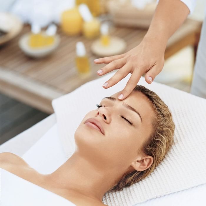 Eine Frau liegt auf einer Massageliege, während eine Hand sanft über ihre Stirn streicht.
