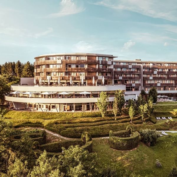 Modernes, mehrstöckiges Gebäude mit Terrassen, umgeben von einer begrünten Landschaft und Bäumen.
