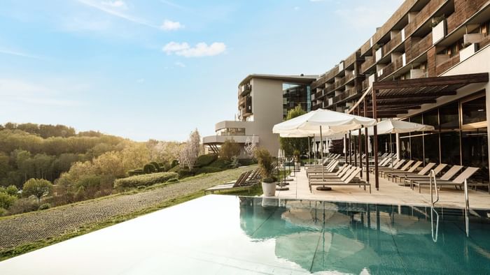 Außenpool eines Resorts mit Liegen, Sonnenschirmen und Gebäude im Hintergrund an einem sonnigen Tag.
