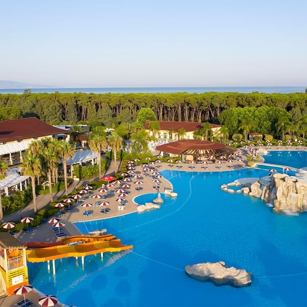Luftaufnahme eines großen Resorts mit Pools, Wasserrutsche, Liegestühlen und Bäumen an der Küste.