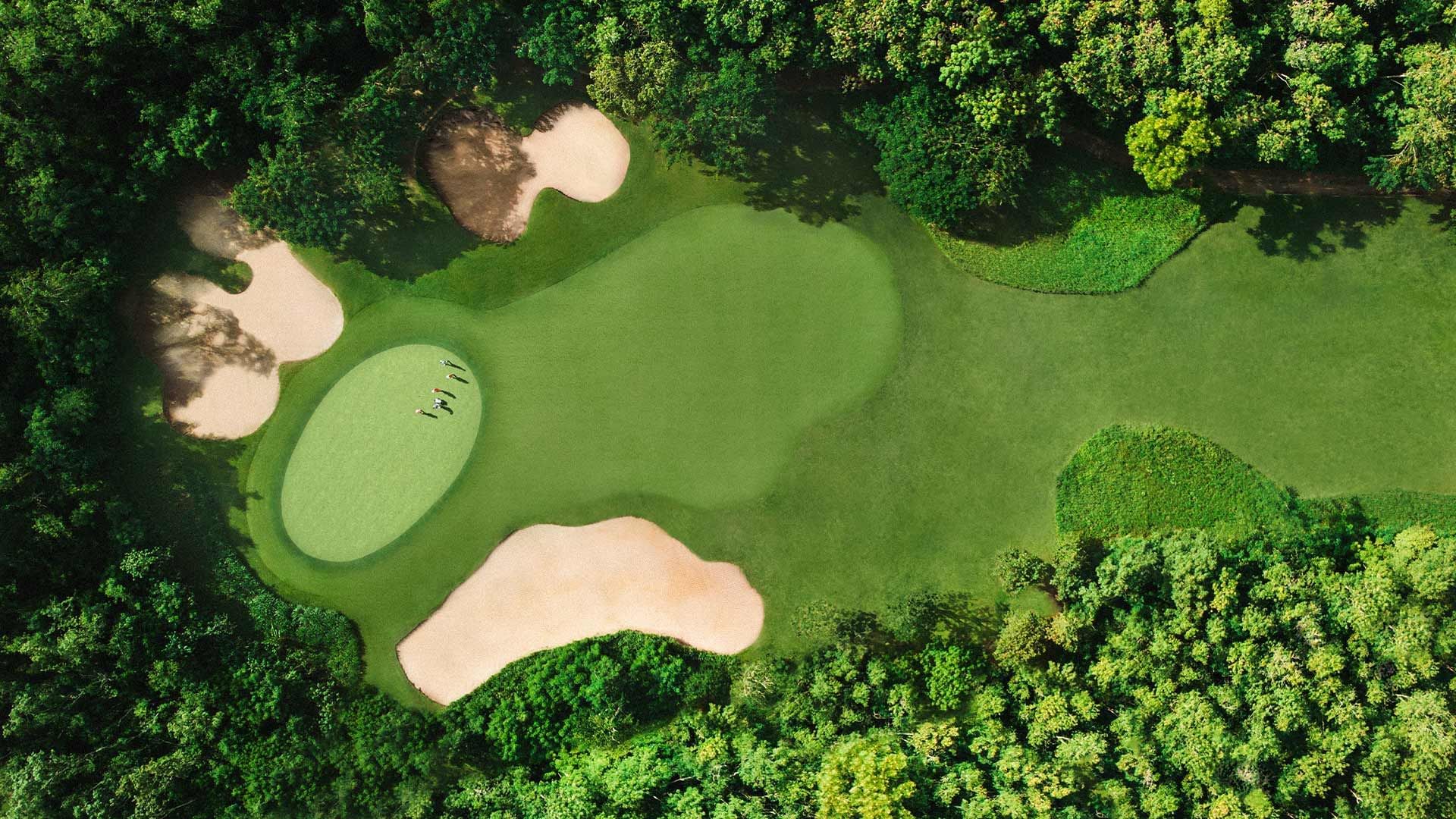 Vista aerea di un campo da golf con buche e bunker, circondato da una fitta vegetazione.