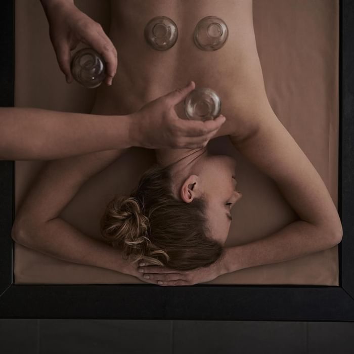 Frau erhält eine Behandlung mit Gläsern auf dem Rücken in einem Wellness-Kontext.