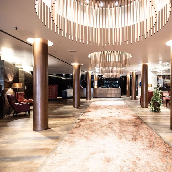 Elegante Hotellobby mit hängenden Kronleuchtern, Sitzbereichen, Empfangstheke und einem Teppich.
