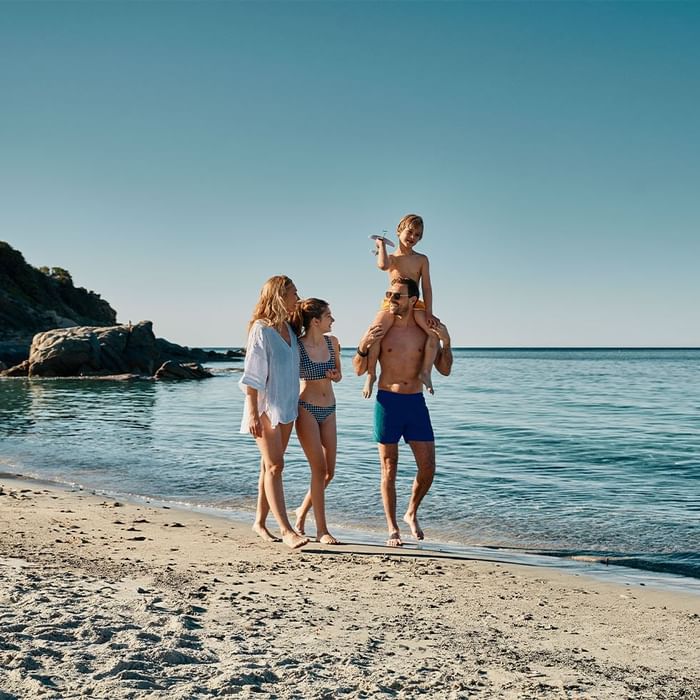 Eine Familie genießt einen Tag am Strand, wobei ein Vater sein Kind auf den Schultern trägt.