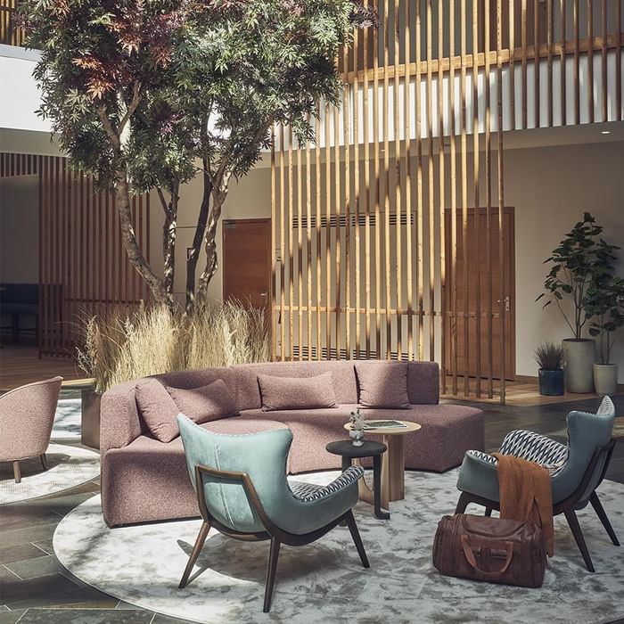 Loungebereich mit Sitzmöbeln, Holzwand, und Baum im Innenhof eines modernen Gebäudes.