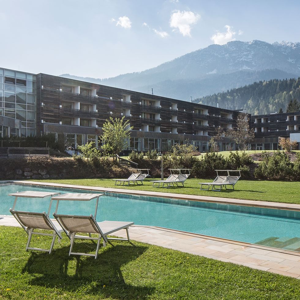 Hotelgebäude mit Pool und Liegestühlen vor einer malerischen Bergkulisse.