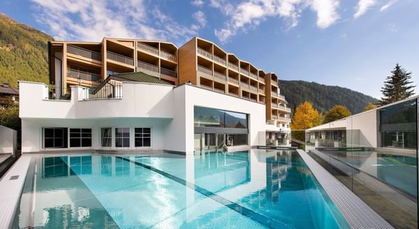 Schwimmbad vor einem Hotel mit mehreren Stockwerken und einem Berg im Hintergrund.