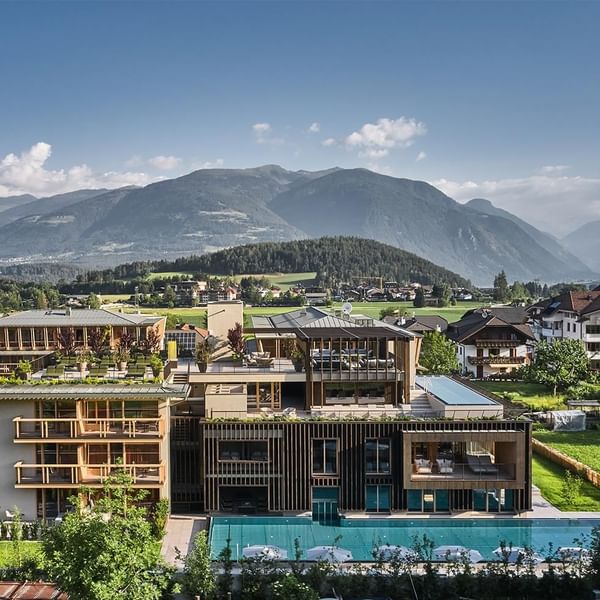 Modernes Hotelkomplex mit Pool, umgeben von Bäumen und Bergen in der Ferne.