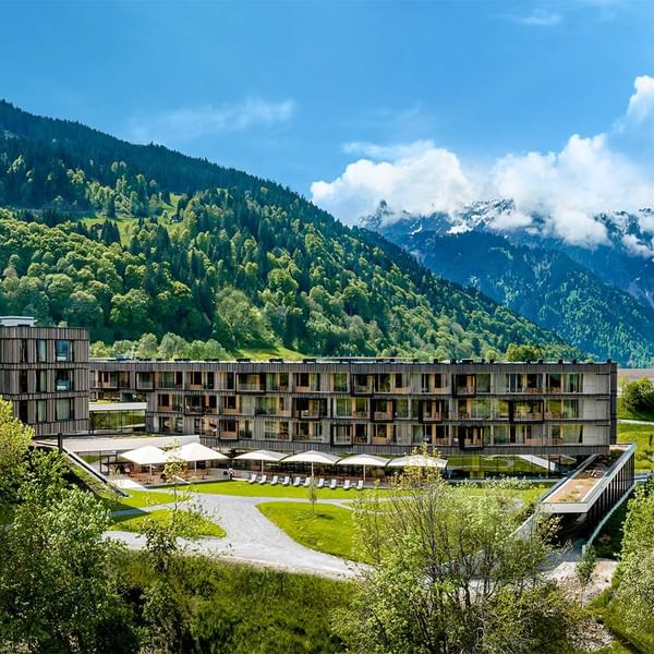Modernes Gebäudekomplex in den Alpen mit grünen Dächern und Liegestühlen vor einer Bergkulisse.