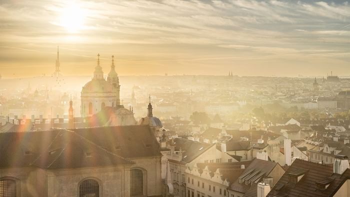 Sonnenaufgang über einer Stadt mit vielen Gebäuden und Türmen, die in warmes Licht getaucht sind.