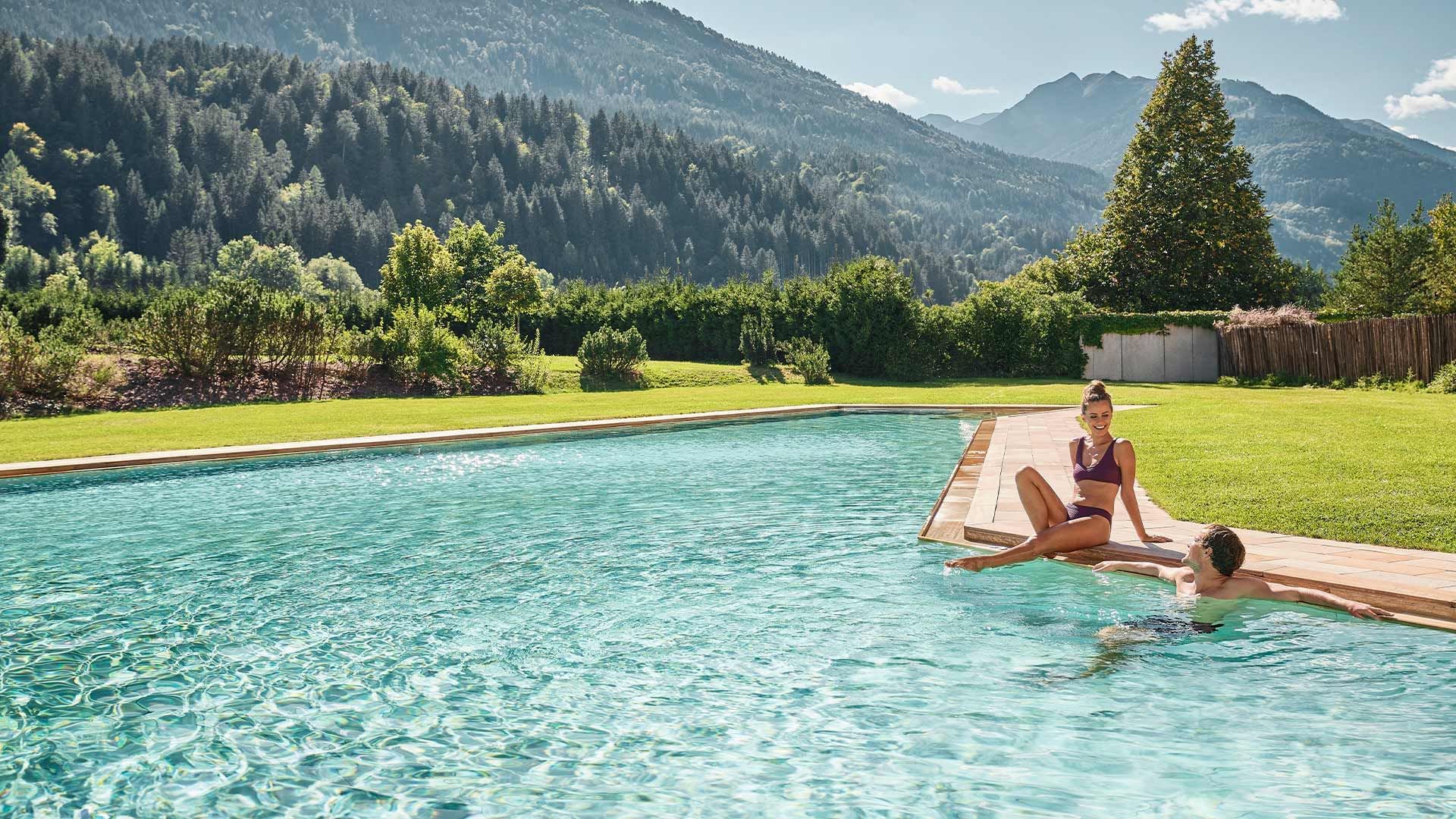 Una coppia si gode una piscina all'aperto con vista sulle montagne e vegetazione circostante.