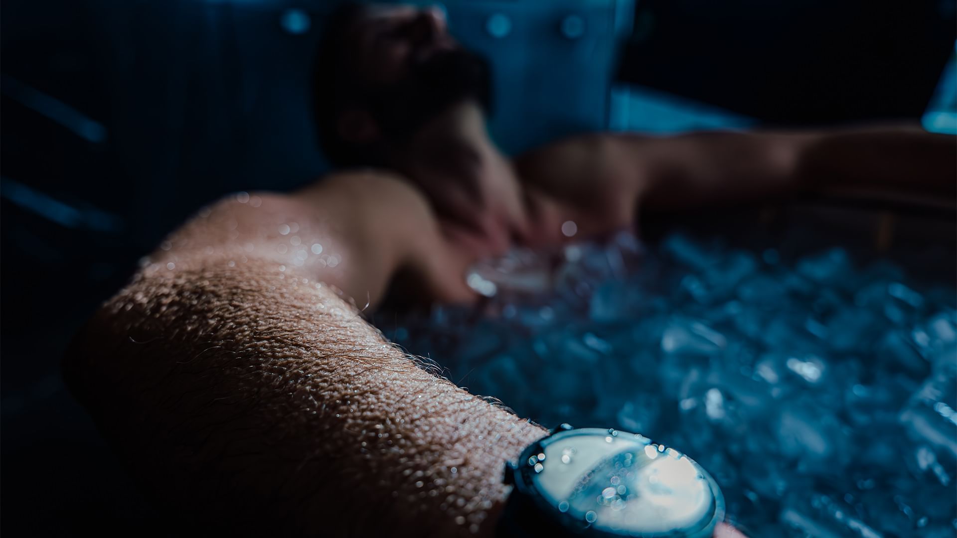 Mann mit Uhr im Arm liegt in einem Jacuzzi mit Wassertropfen auf dem Handgelenk.