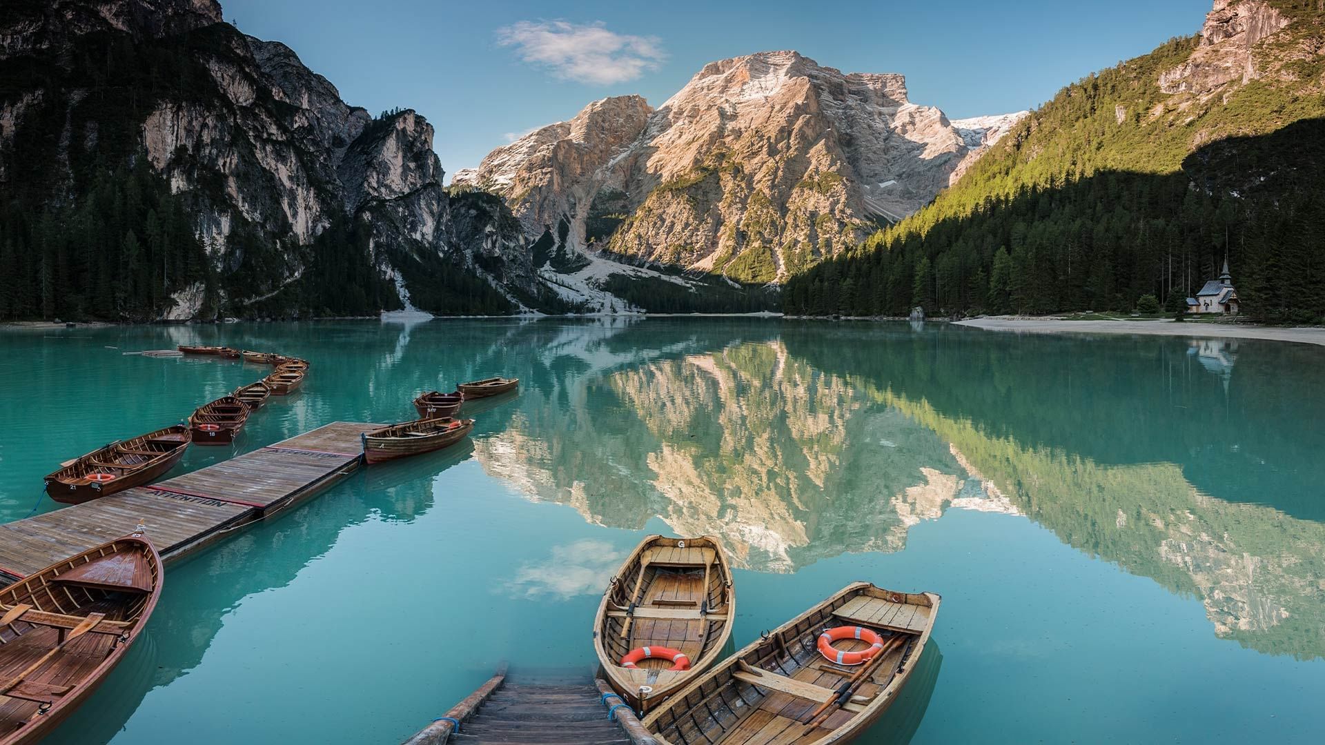 Mehrere Boote am Steg eines Bergsees, umgeben von hohen Bergen und dichten Wäldern.