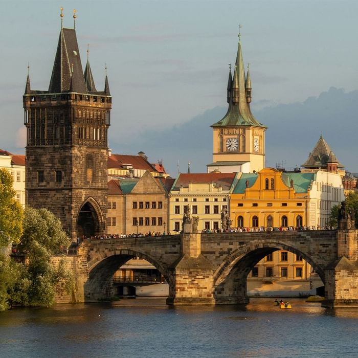 Steinbrücke über Wasser mit Turm und Uhr im Hintergrund, viele Menschen auf der Brücke.