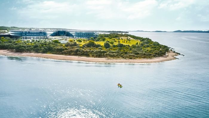 Luftaufnahme eines Küstenresorts mit Gebäuden, grüner Landschaft und einer gelben Kanu im Wasser.