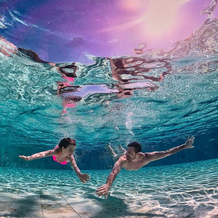 Unterwasseraufnahme eines Paares, das im Pool schwimmt und sich gegenseitig die Hände berührt.