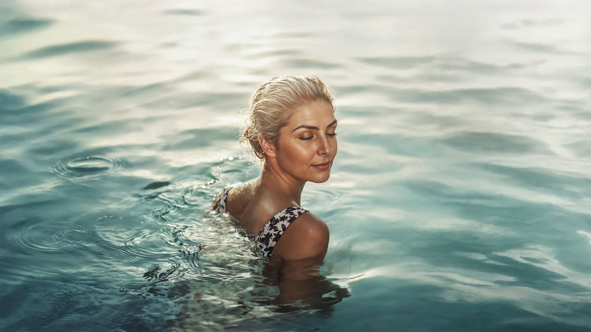 Blondhaarige Frau in einem schwarzen und weißen Bikini im Wasser mit geschlossenen Augen.