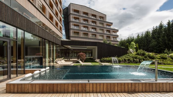 Schwimmbad vor einem modernen Gebäude, umgeben von Bäumen und Liegen.
