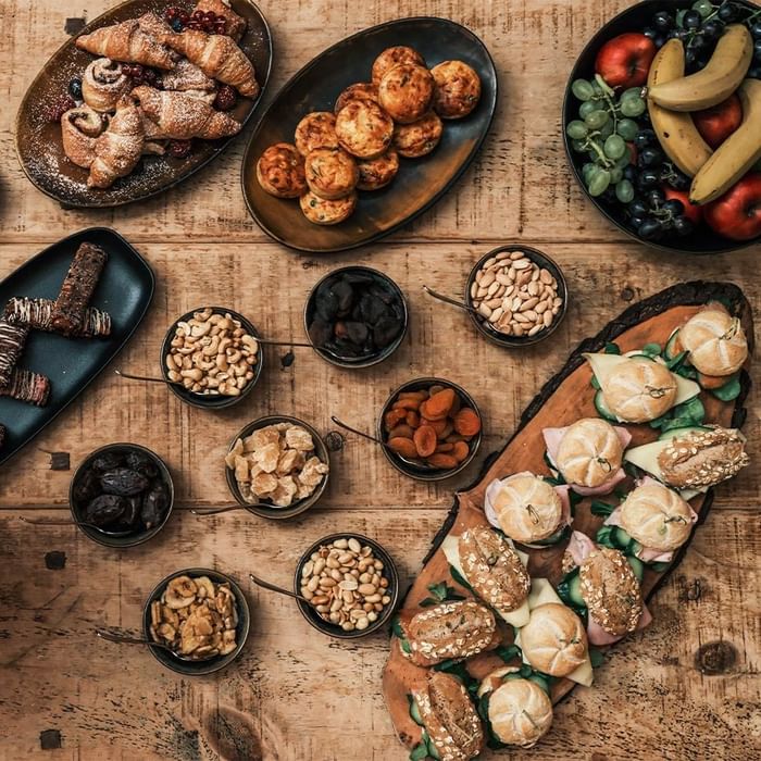Verschiedene Snacks und Früchte auf einem hölzernen Tisch angeordnet, darunter Croissants, Nüsse und Früchte.