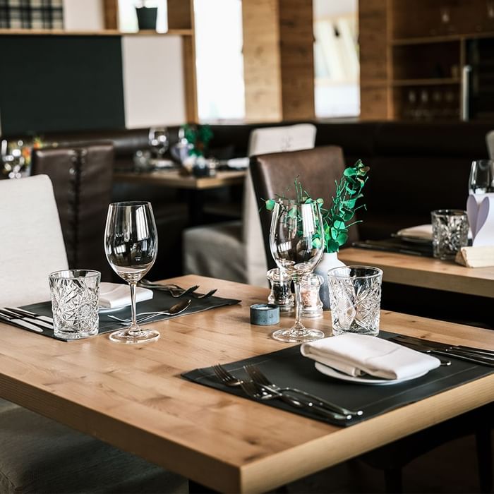 Tavolo da pranzo in legno con posate, bicchieri, tovaglioli e piante in un ristorante.