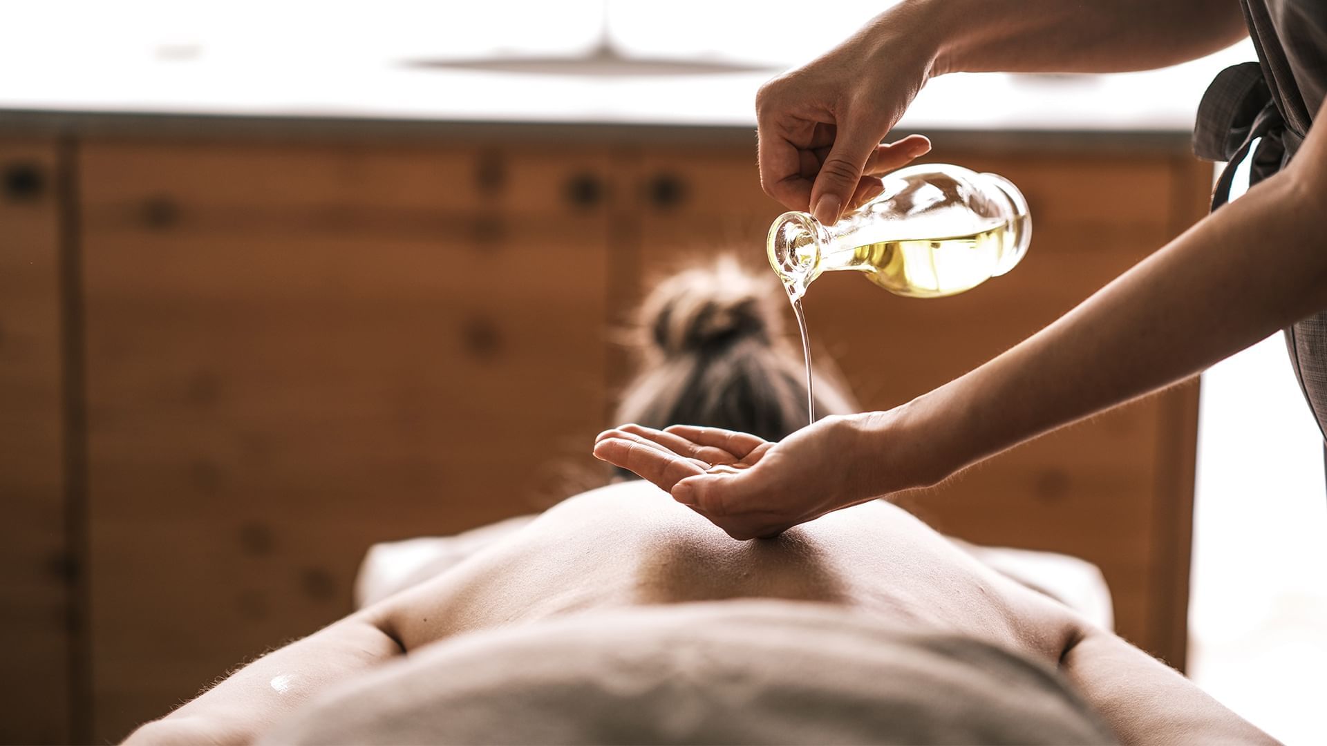 Una persona riceve un massaggio con olio versato sul suo corpo da un massaggiatore.