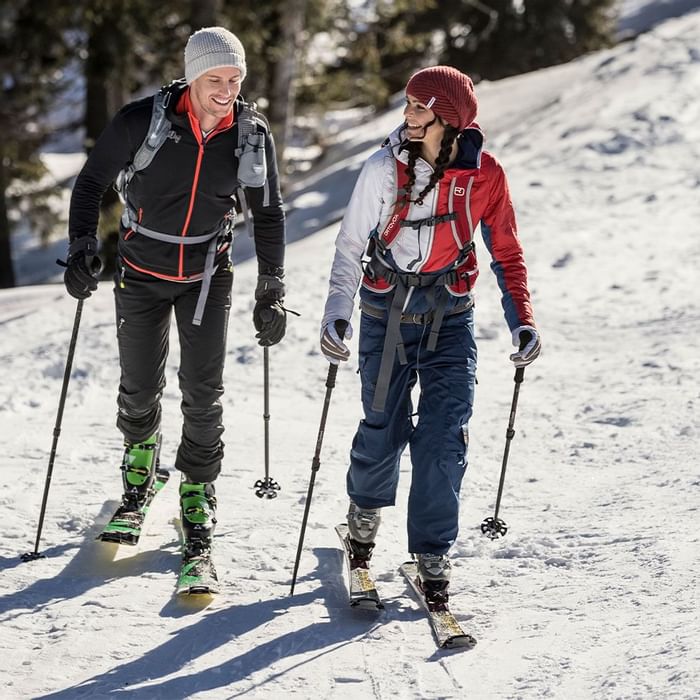 Ein Paar beim Skiwandern, Mann in schwarzer und Frau in roter Jacke, beide mit Rucksäcken.