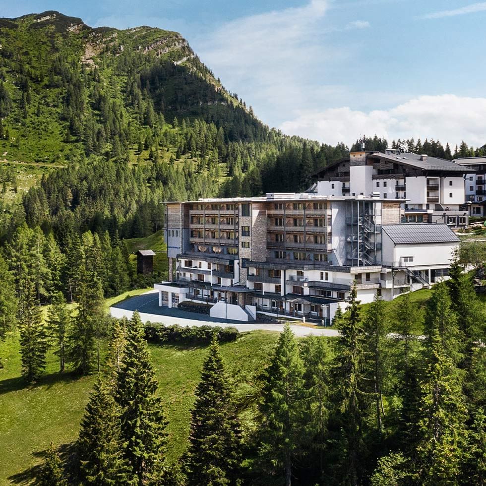 Großes, modernes Gebäudekomplex inmitten eines bewaldeten, grünen Berghangs.