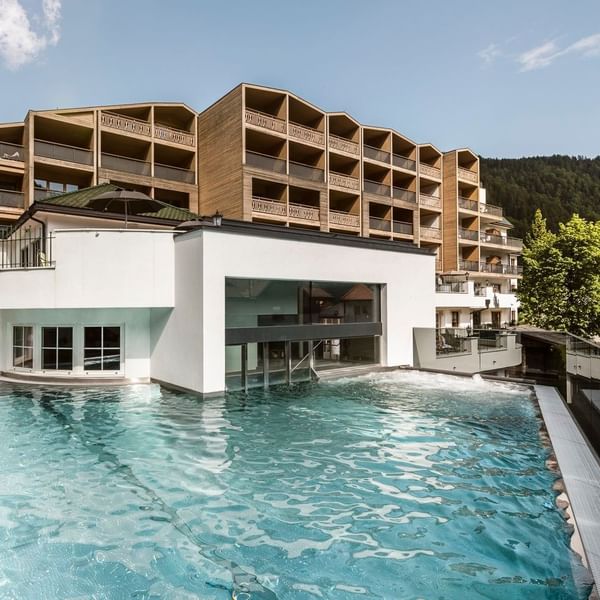 Modernes Hotelgebäude mit angrenzendem Swimmingpool und umgebenden Wäldern unter einem klaren Himmel.