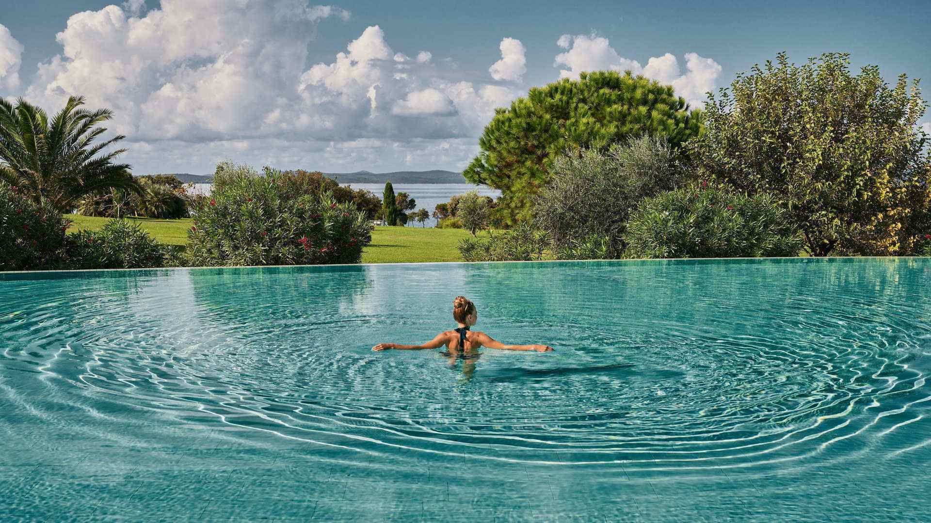 Frau schwimmt in einem großen, kreisförmigen Pool mit umgebender Natur und Meerblick.