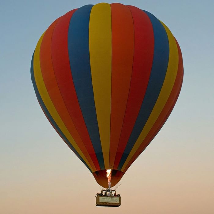Heißluftballon in Blau, Gelb, Rot und Orange mit Passagieren unter dem Ballonkorb, der in der Luft schwebt.