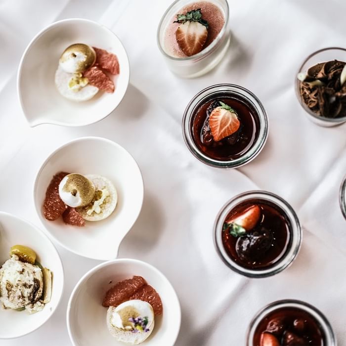 Verschiedene Desserts in kleinen Gläsern und Schalen, darunter Erdbeeren und Schokoladencreme.