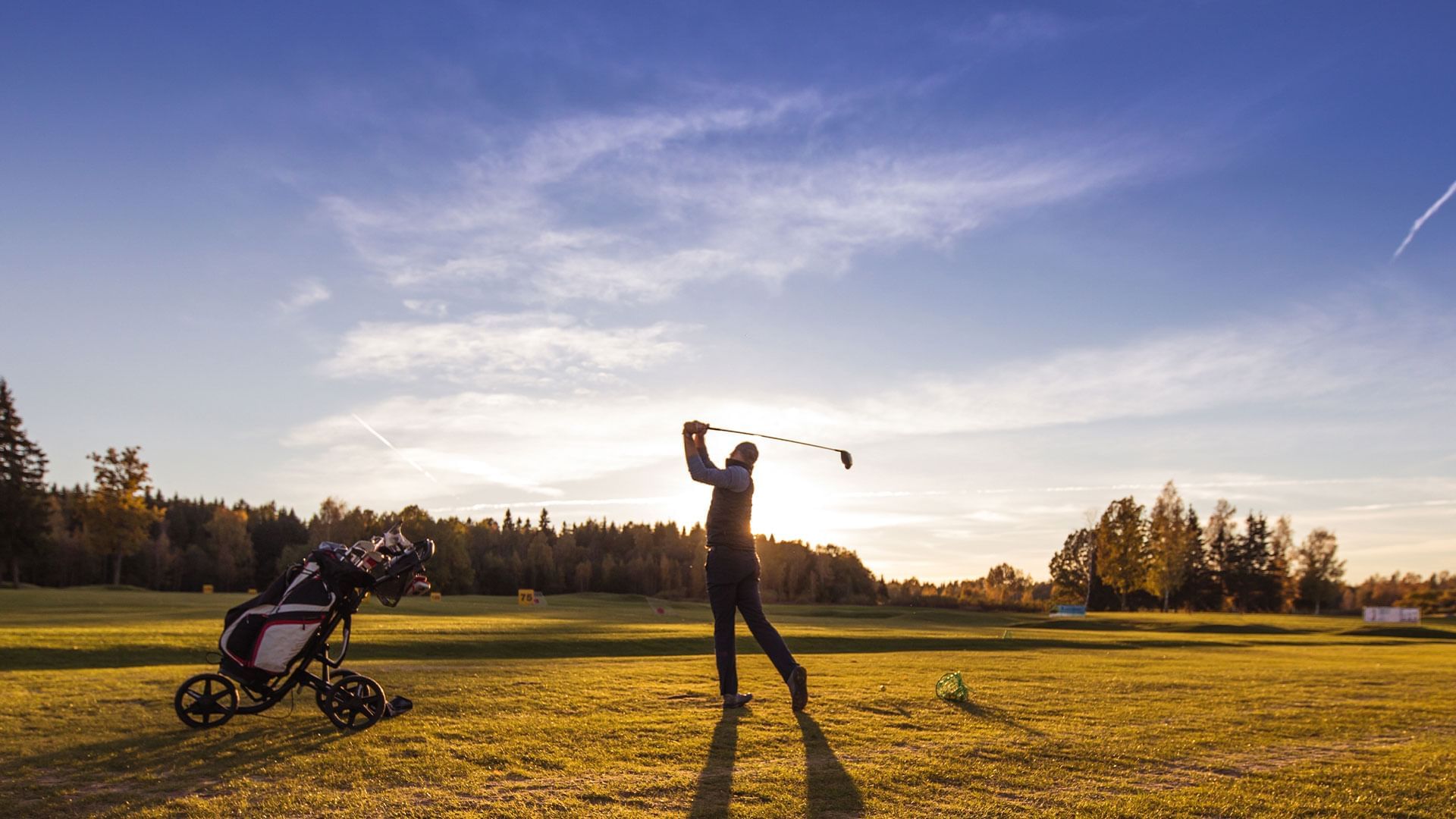 Giocatore di golf che colpisce la palla con il bastone sul campo da golf al tramonto.