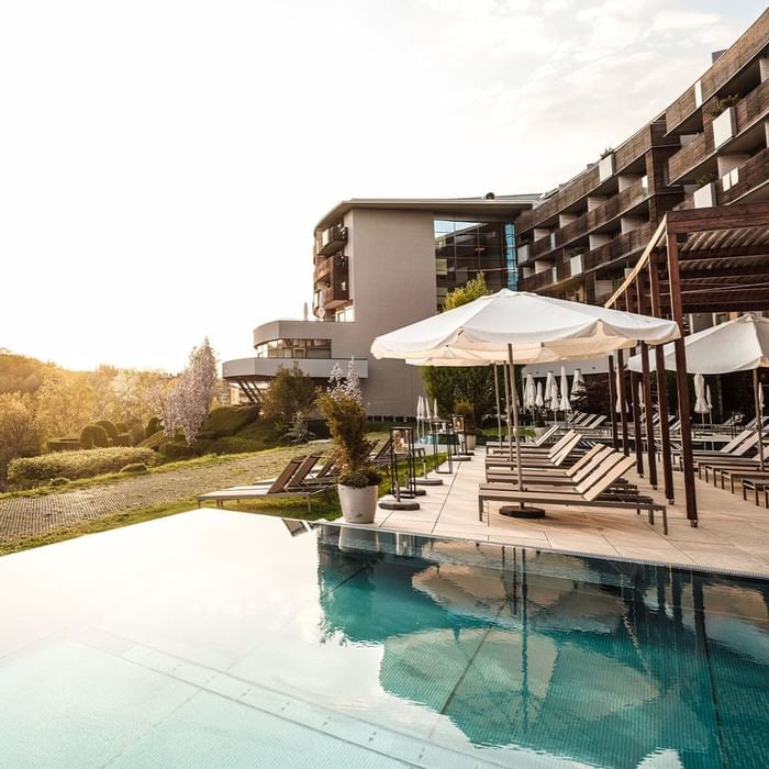 Hotel-Pool mit Liegen, Sonnenschirmen und Gebäude im Hintergrund bei Sonnenuntergang.