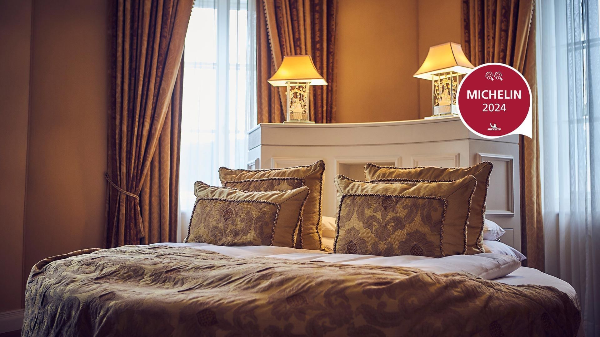 Elegantes Hotelzimmer mit großem Bett, vier Kissen, zwei Nachtlampen und einem Michelin-Logo 2024.