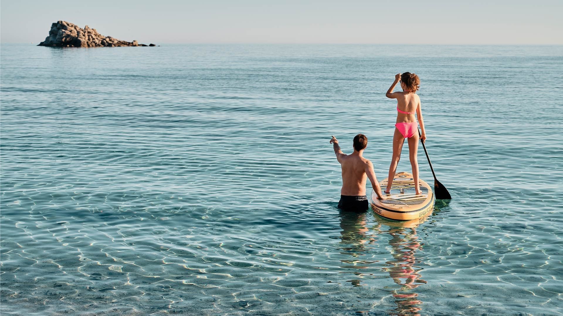 Zwei Personen auf einem Paddelboard im Meer, eine paddelt und die andere steht.