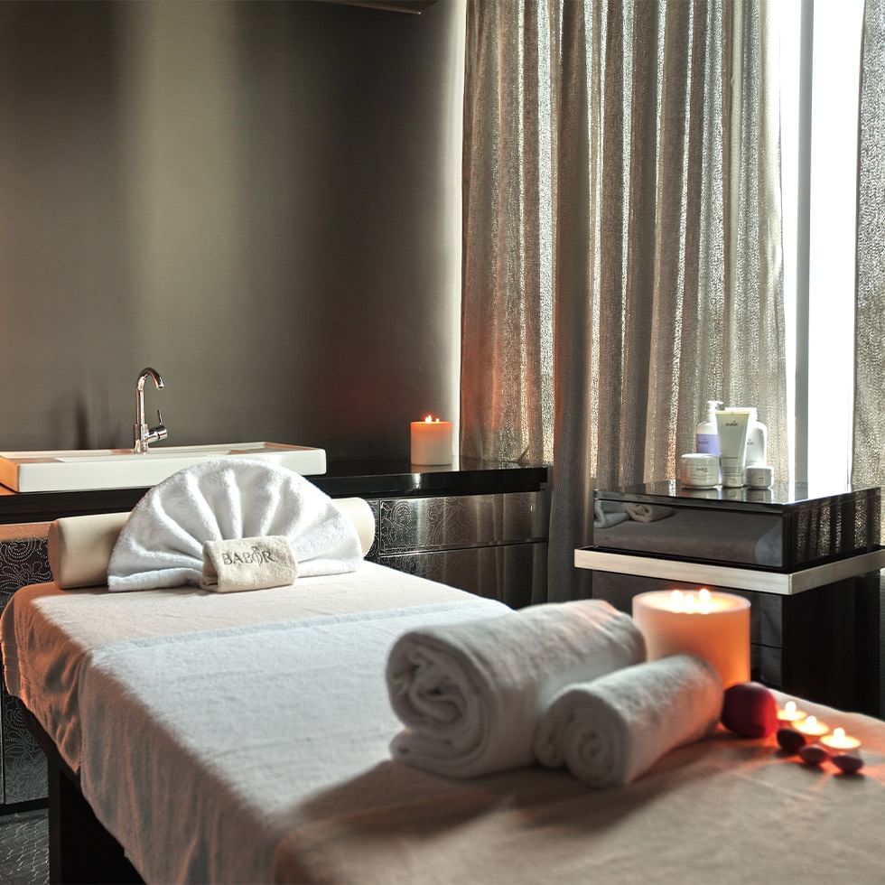 Eine Massageliege mit Handtüchern, Kerzen und einem Waschbecken in einem Spa-Zimmer.