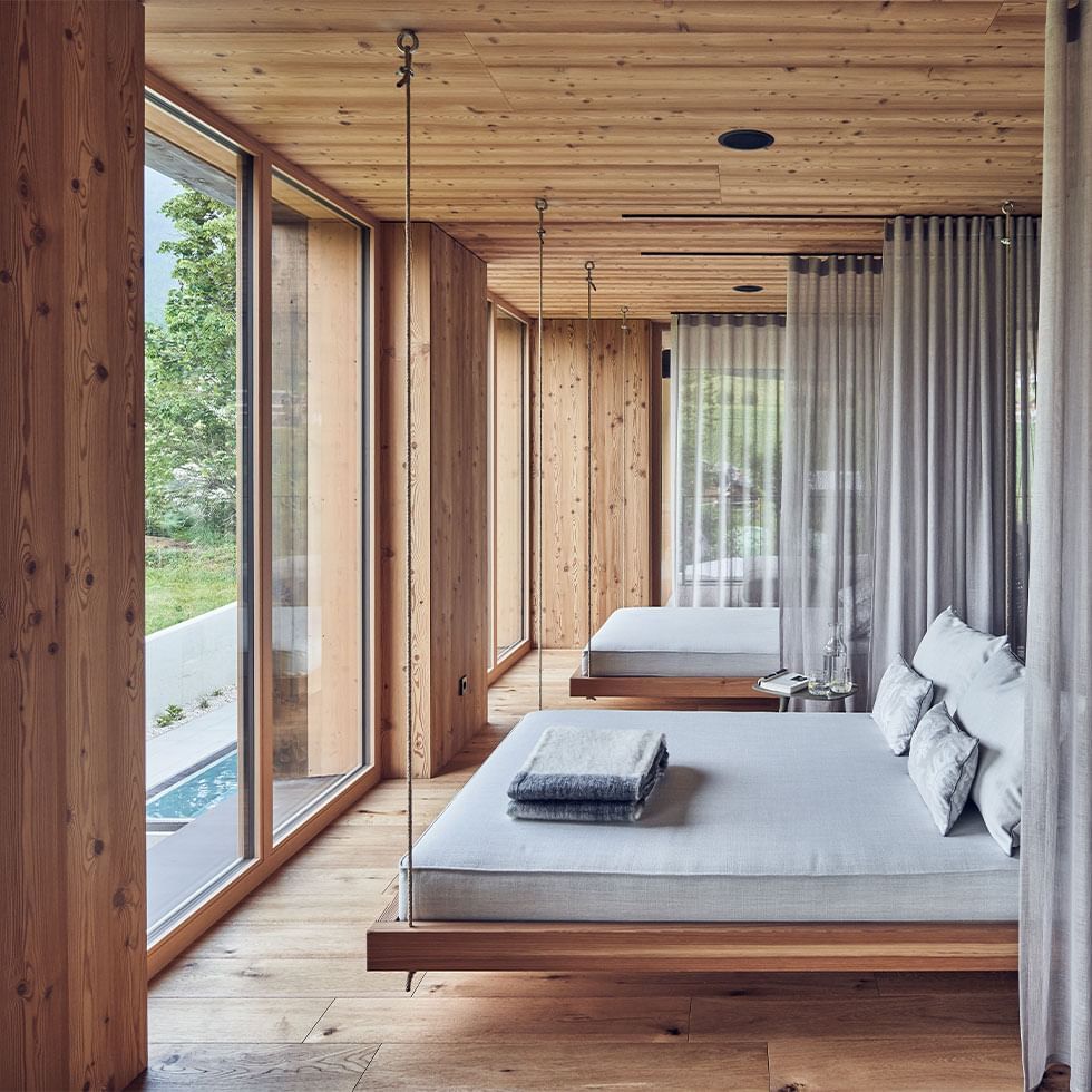 Zwei Hängebetten in einem hellen, hölzernen Schlafzimmer mit großen Fenstern und Gartenblick.